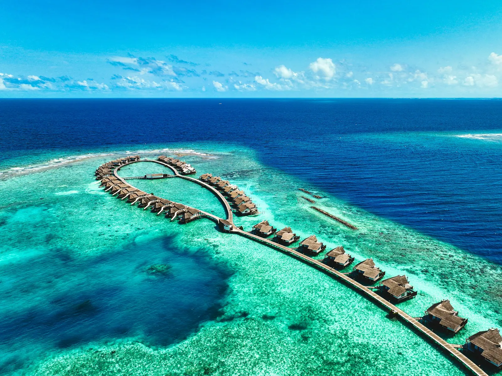 Aerial view of an island resort ringed by overwater villas in the Maldives